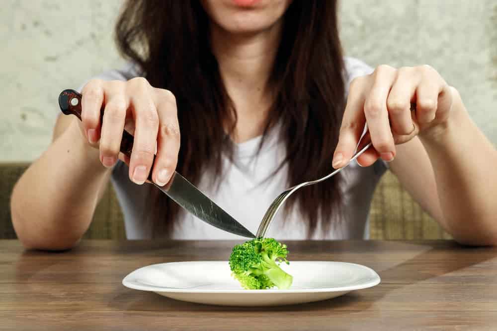 woman using a knife and fork to eat broccoli