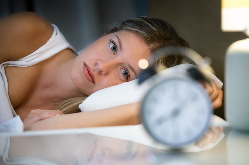 woman in bed looking at her alarm clock